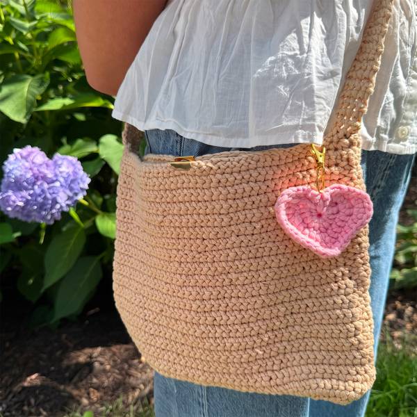 The heart charm clipped to a tan crochet shoulder bag